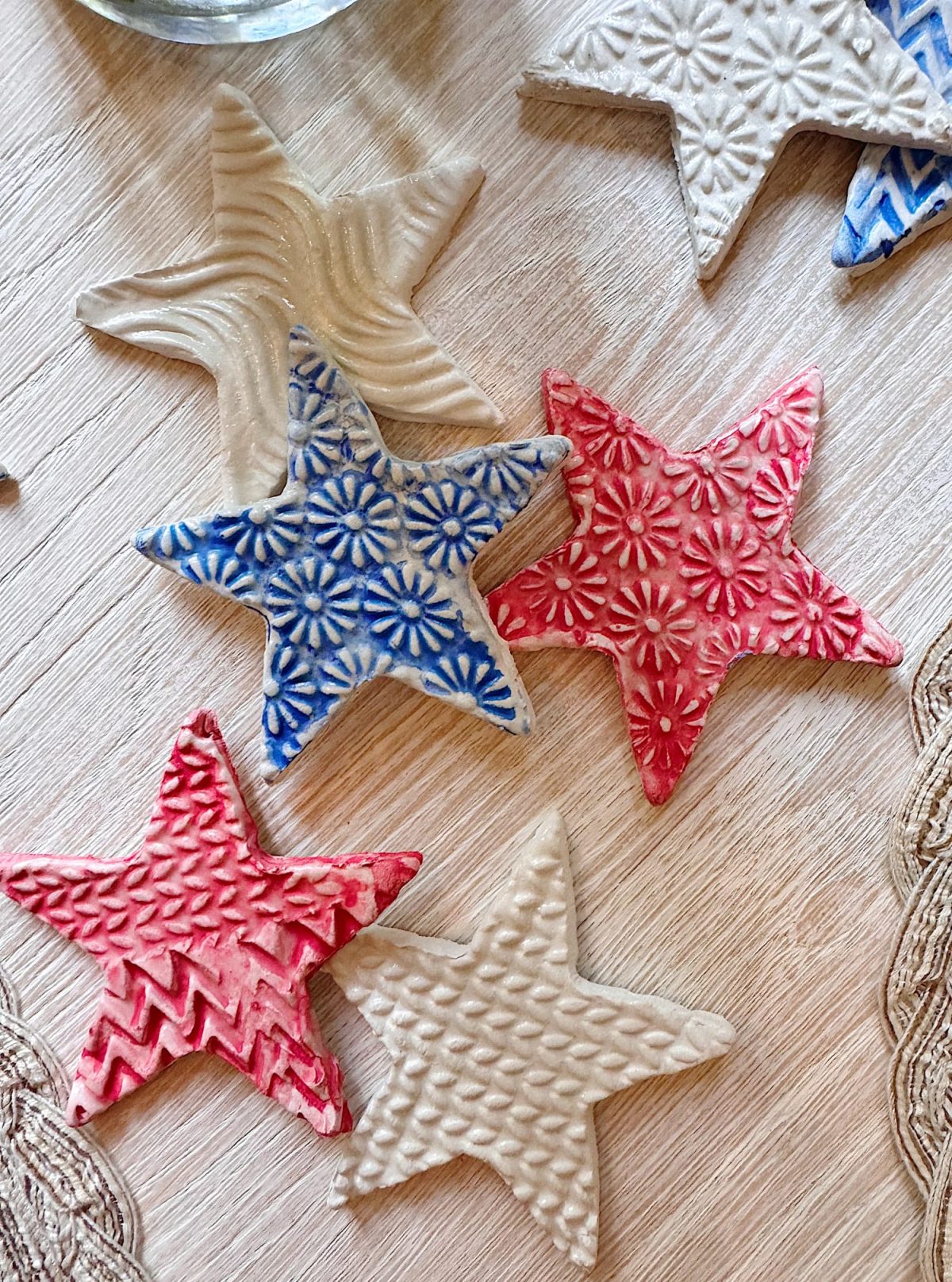 Star-shaped clay ornaments with embossed patterns in red, blue, and white colors are arranged on a light wooden surface.