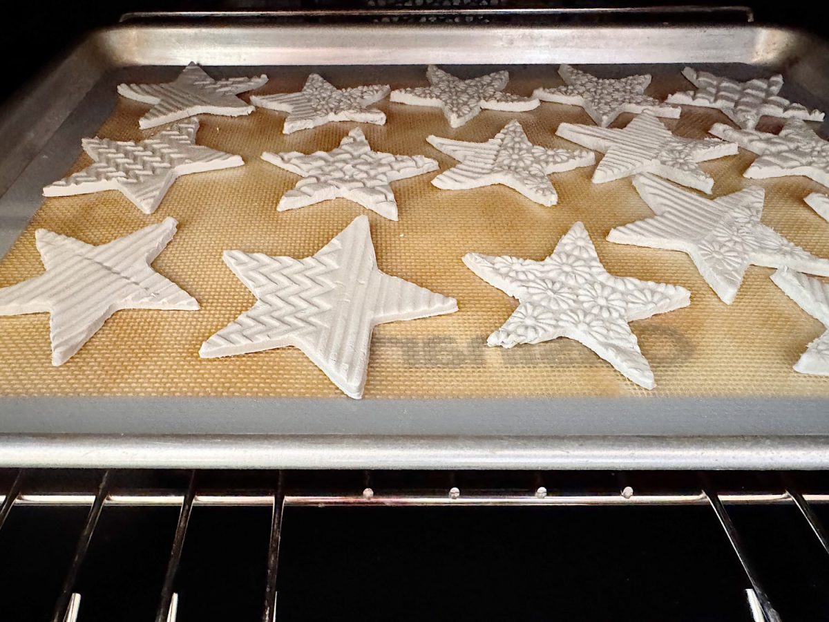 Unbaked clay star ornaments with textured patterns are arranged on a baking tray lined with a silicone mat inside an oven.