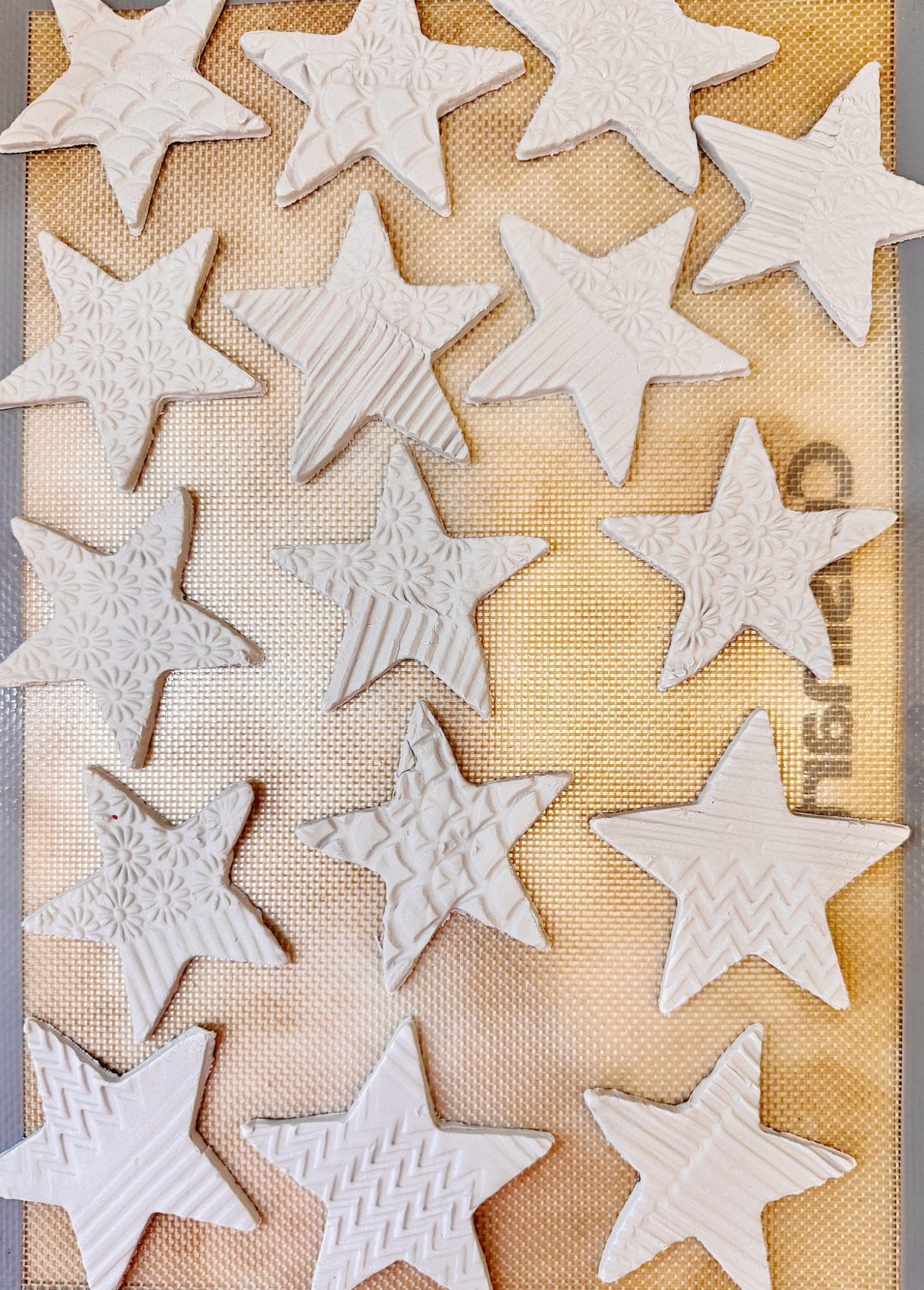 White star-shaped ornaments with embossed patterns are arranged on a baking mat in a grid-like pattern.