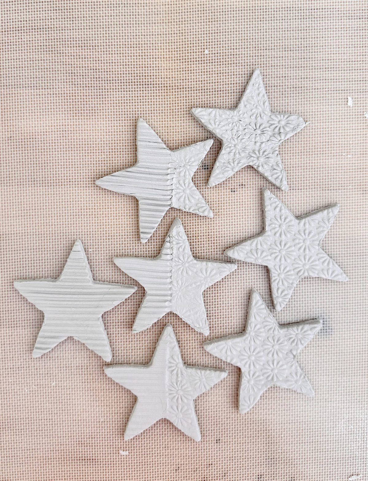 Seven white clay star shapes with different textured patterns are arranged on a light-colored, mesh-like surface.