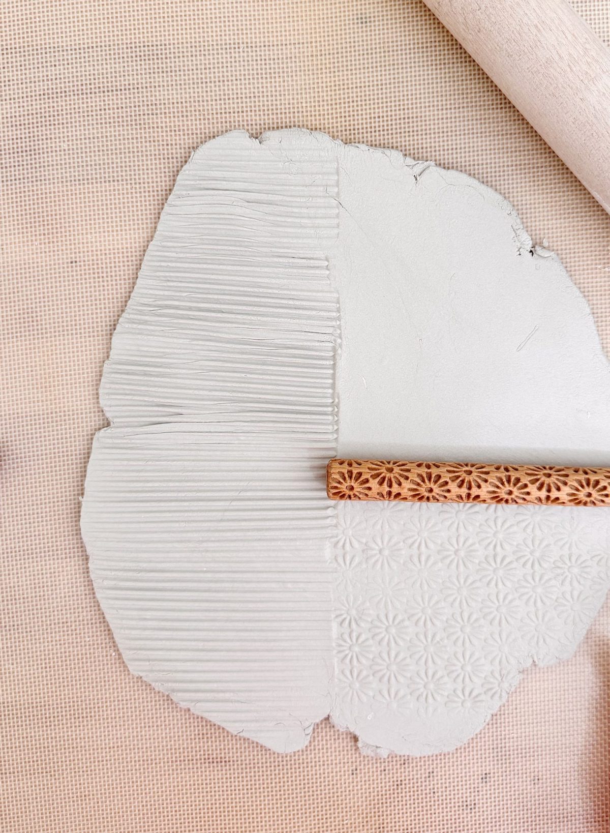 A sheet of clay is being textured with a patterned rolling pin, showing two different patterns on the surface.