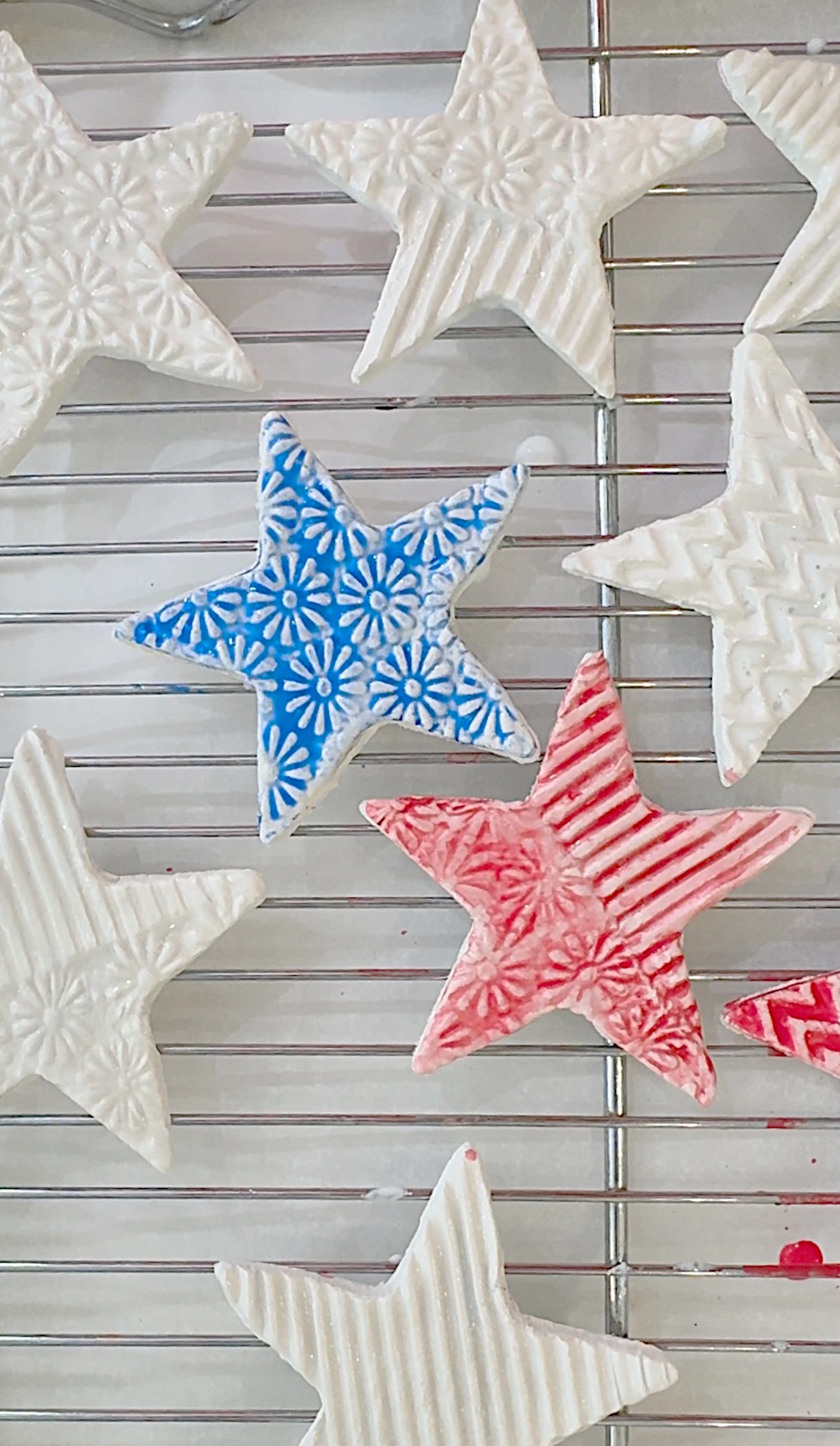 Star-shaped cookies with textured patterns, some decorated in blue or red, are cooling on a metal wire rack.