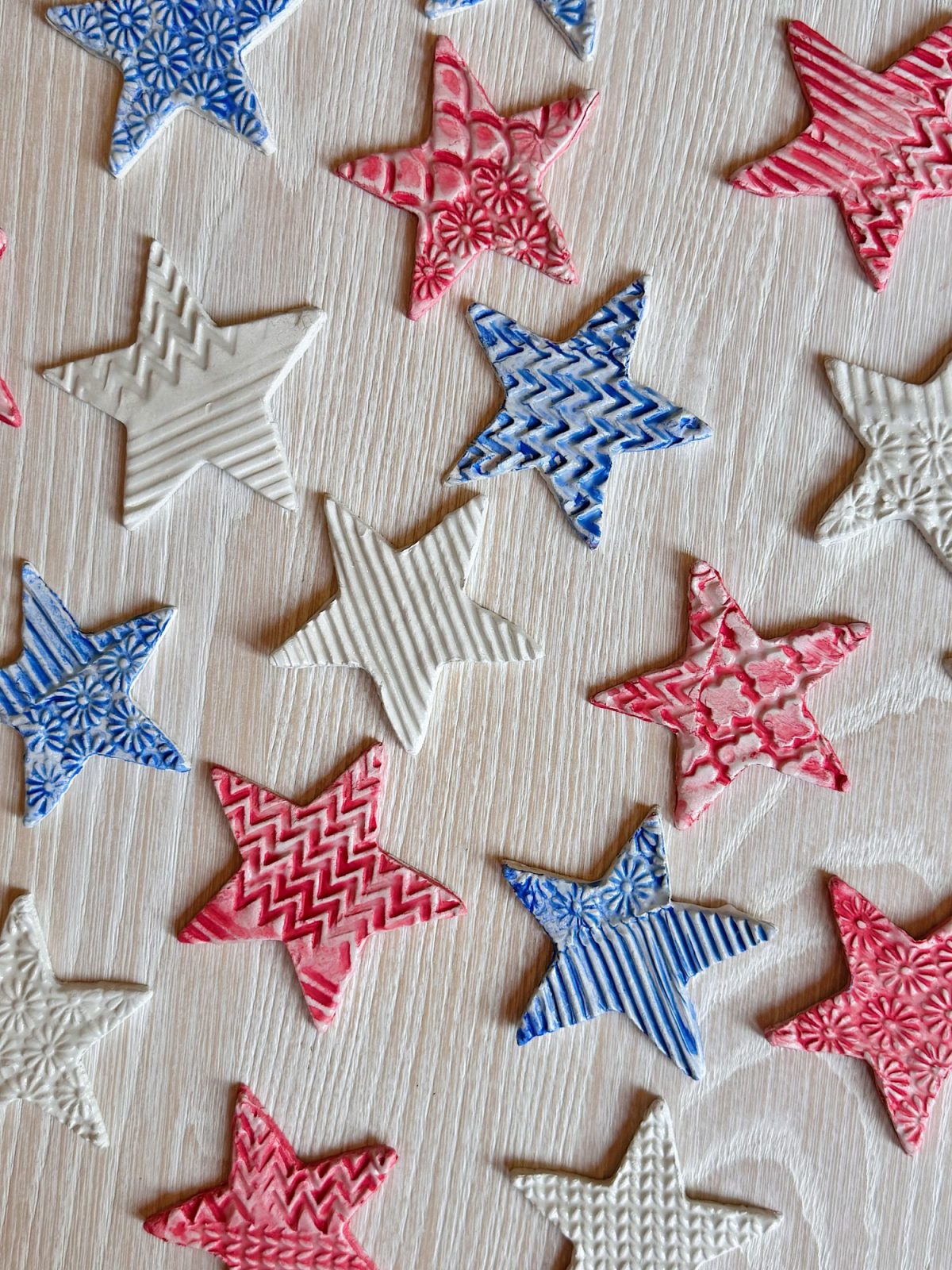 Red, white, and blue star-shaped decorations with textured patterns are arranged on a light wooden surface.