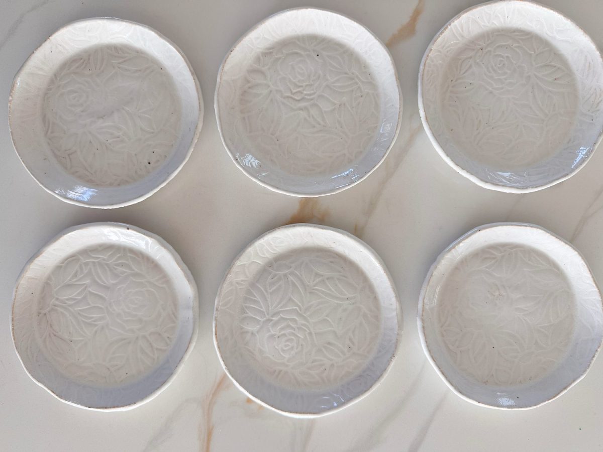 Six white ceramic plates with embossed floral patterns are arranged in two rows of three on a light-colored surface.