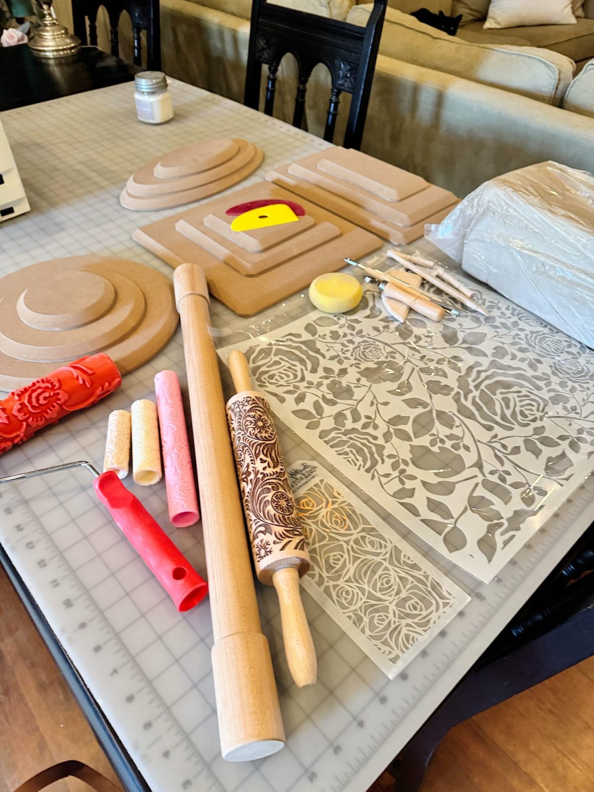 A table displays pottery and clay sculpting tools, rolling pins, textured mats, stencils with floral patterns, and a block of clay ready for crafting.