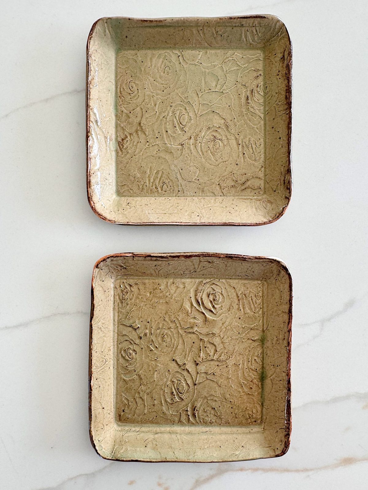 Two rectangular ceramic trays with a floral embossed pattern, placed side by side on a light-colored surface.