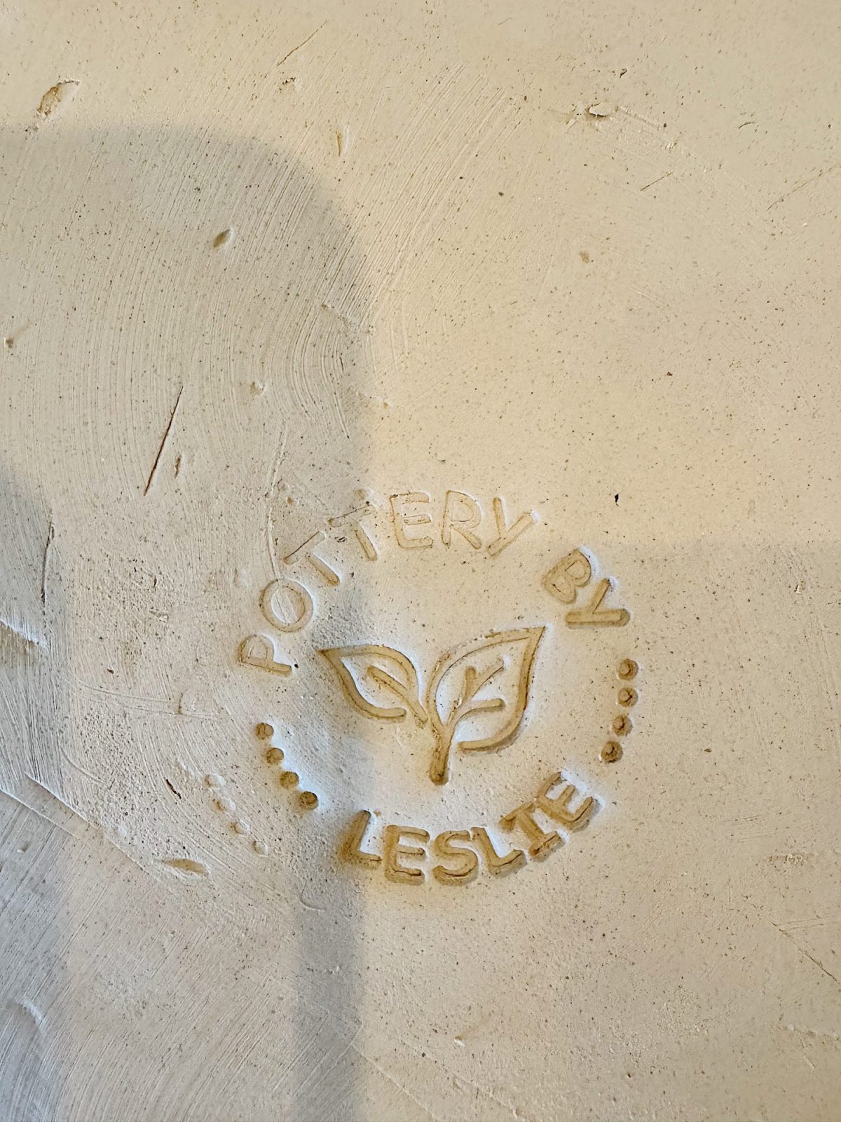 Embossed stamp on clay reads "Pottery by Leslie" with a simple leaf design in the center.