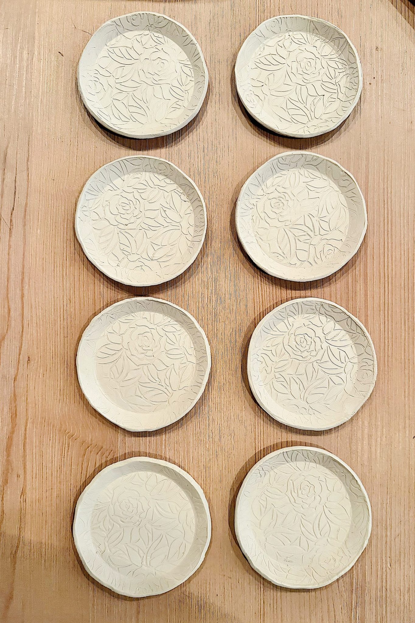 Eight round ceramic plates with embossed floral patterns are arranged in two vertical columns on a wooden surface.