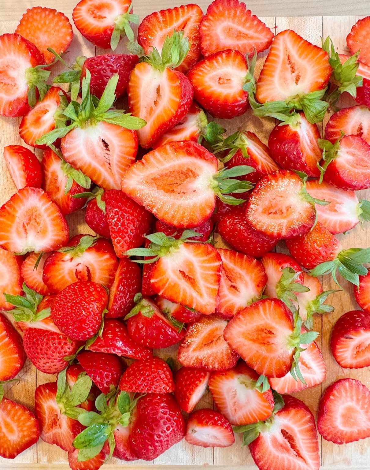 A pile of fresh strawberries, some whole and some cut in half, displayed on a wooden surface.