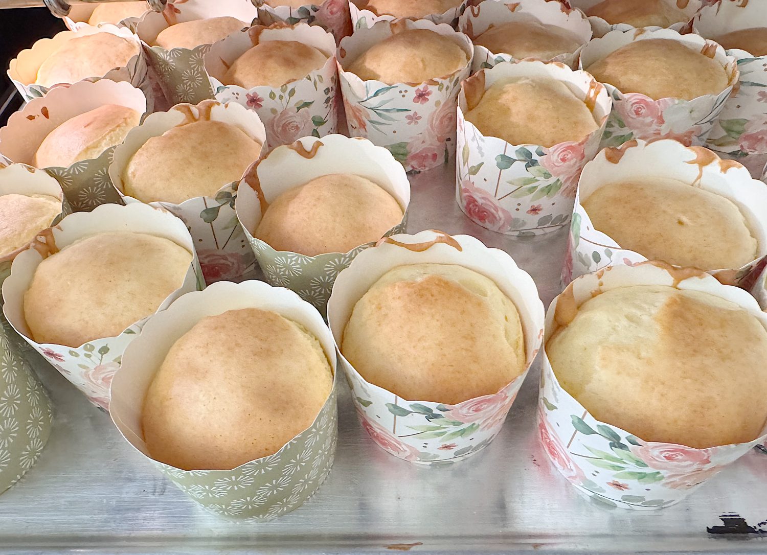 Several freshly baked sponge cakes in floral paper cups arranged on a baking tray.