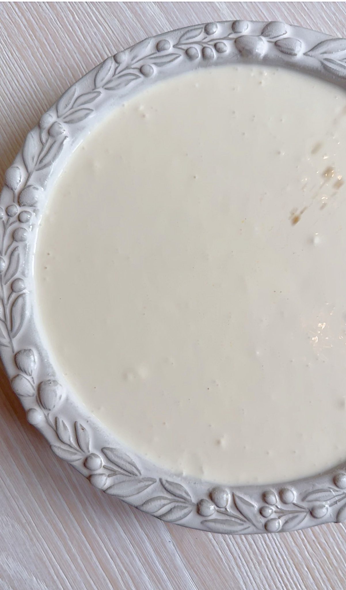 A white ceramic plate filled with a smooth, creamy white liquid or sauce, placed on a pale wooden surface.