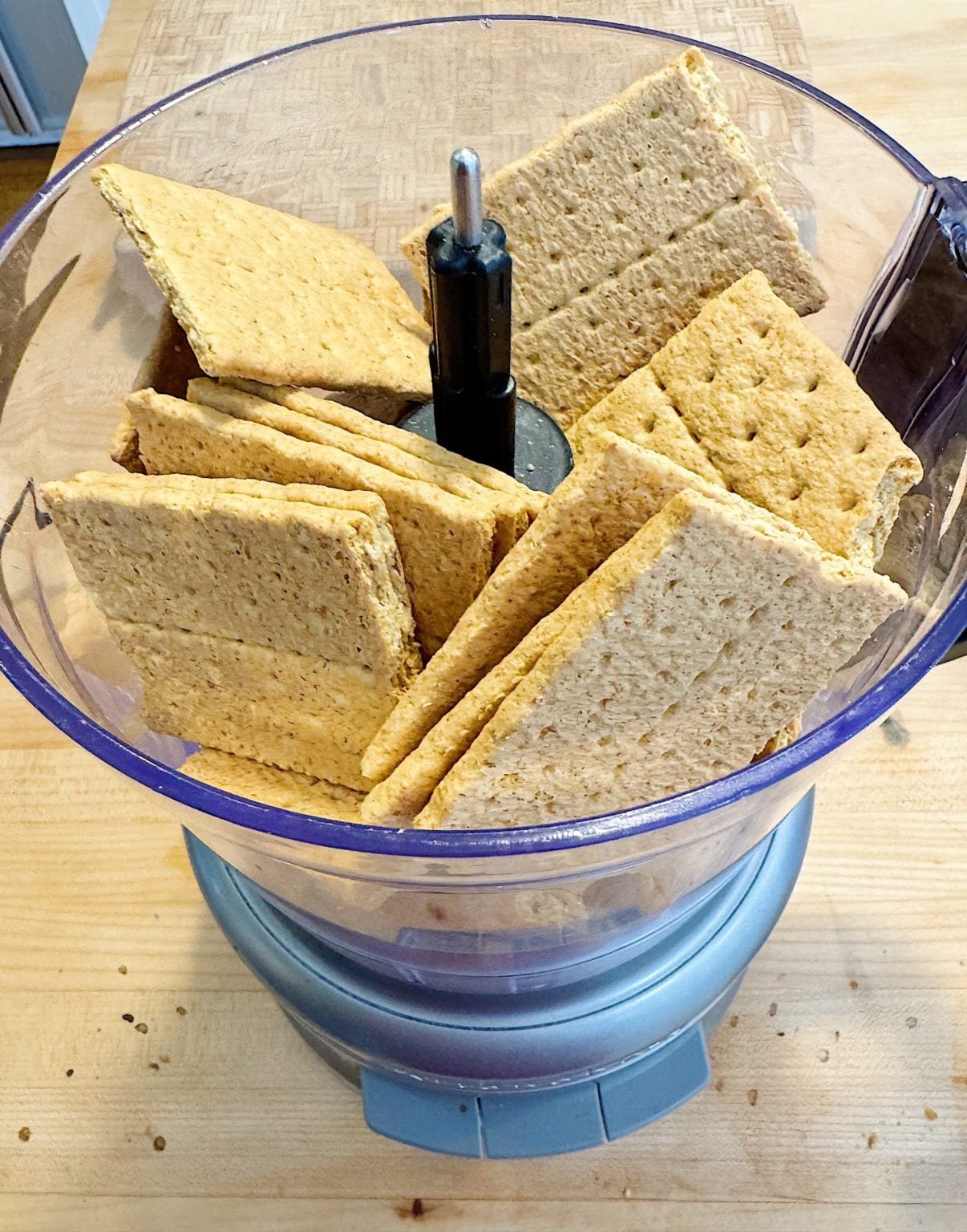 A food processor filled with whole graham crackers on a wooden countertop, ready for processing.