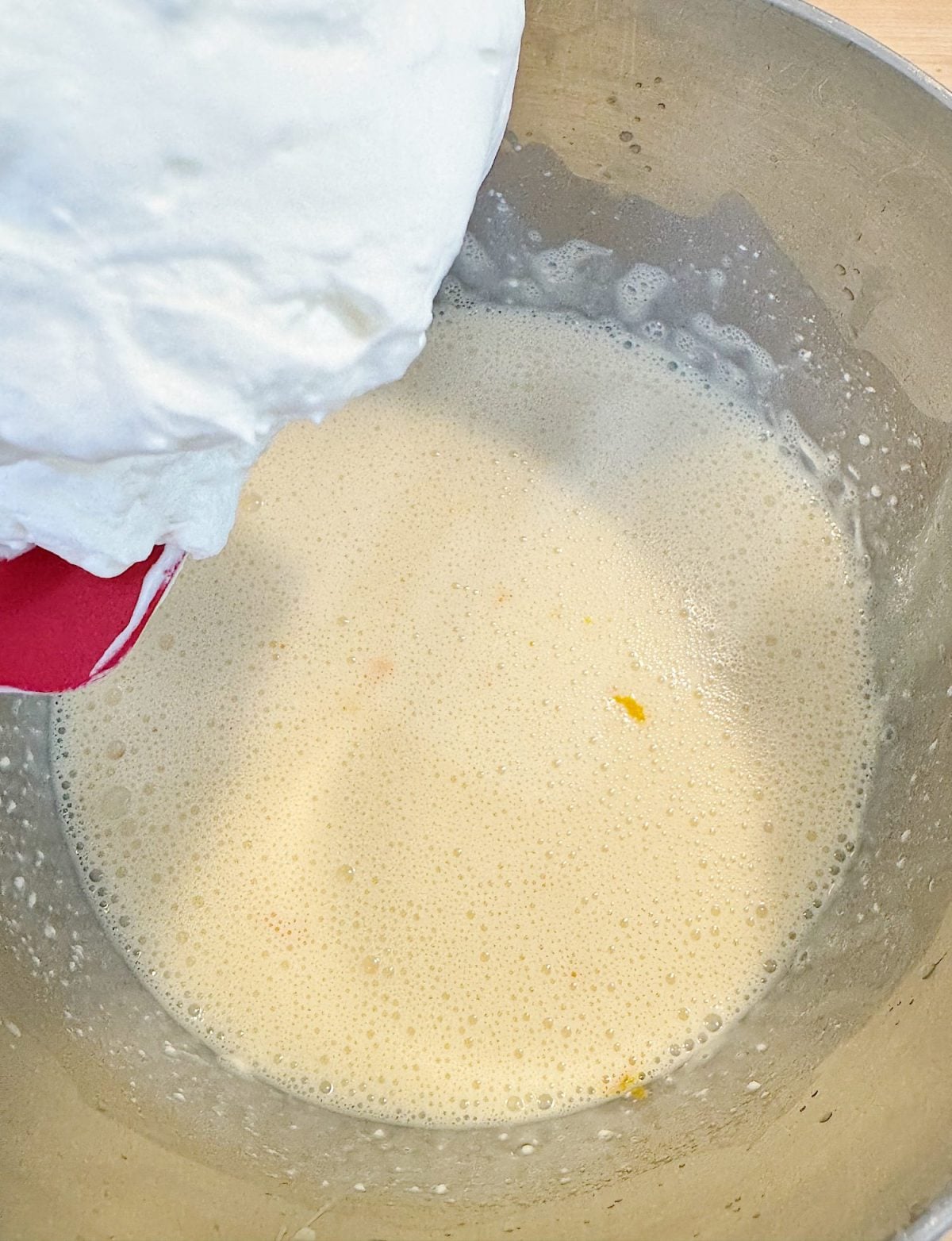 A mixing bowl with a pale yellow batter and whipped egg whites being folded in with a spatula.