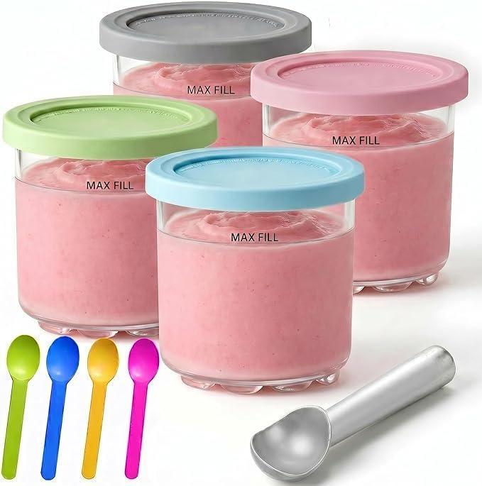 Four glass jars with pastel-colored lids filled with pink frozen dessert, made effortlessly using the Ninja Creami, four colorful spoons, and a metal scoop are arranged on a white surface.