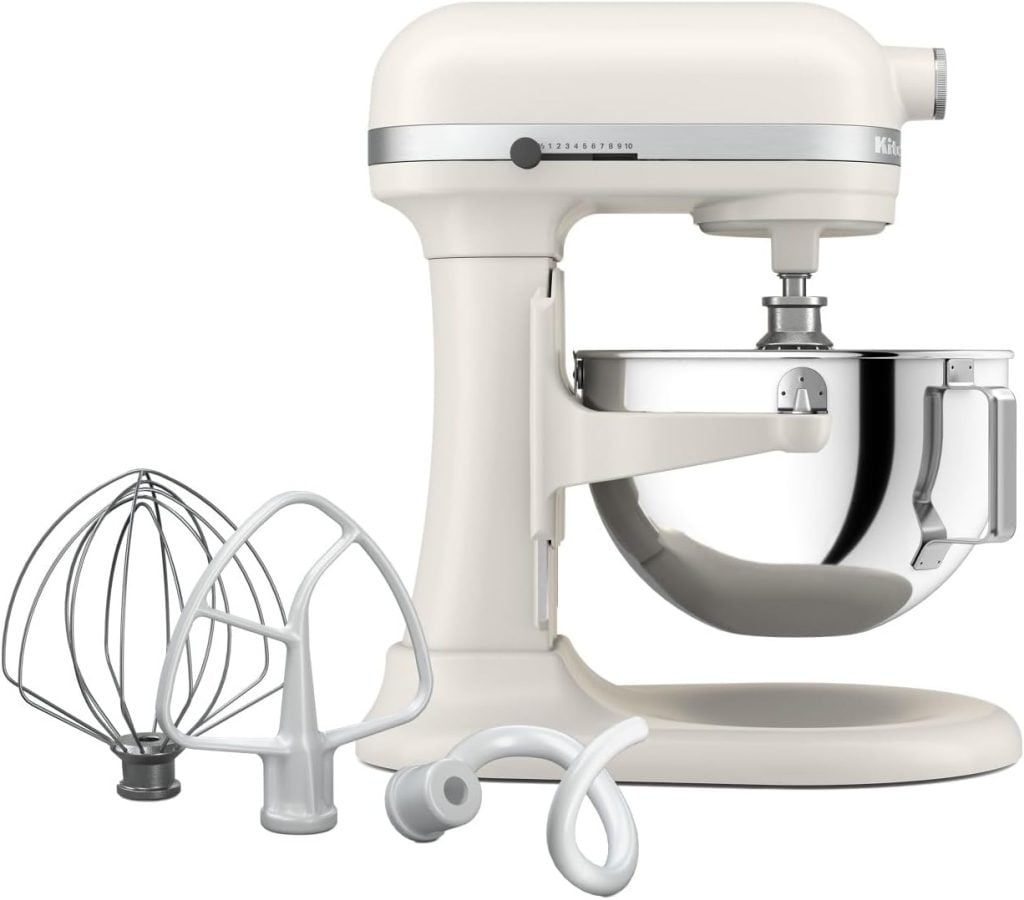 A white stand mixer with a stainless steel mixing bowl, shown with three attachments—a wire whisk, flat beater, and dough hook—placed in front. Perfect for Amazon Prime Day kitchen upgrades.