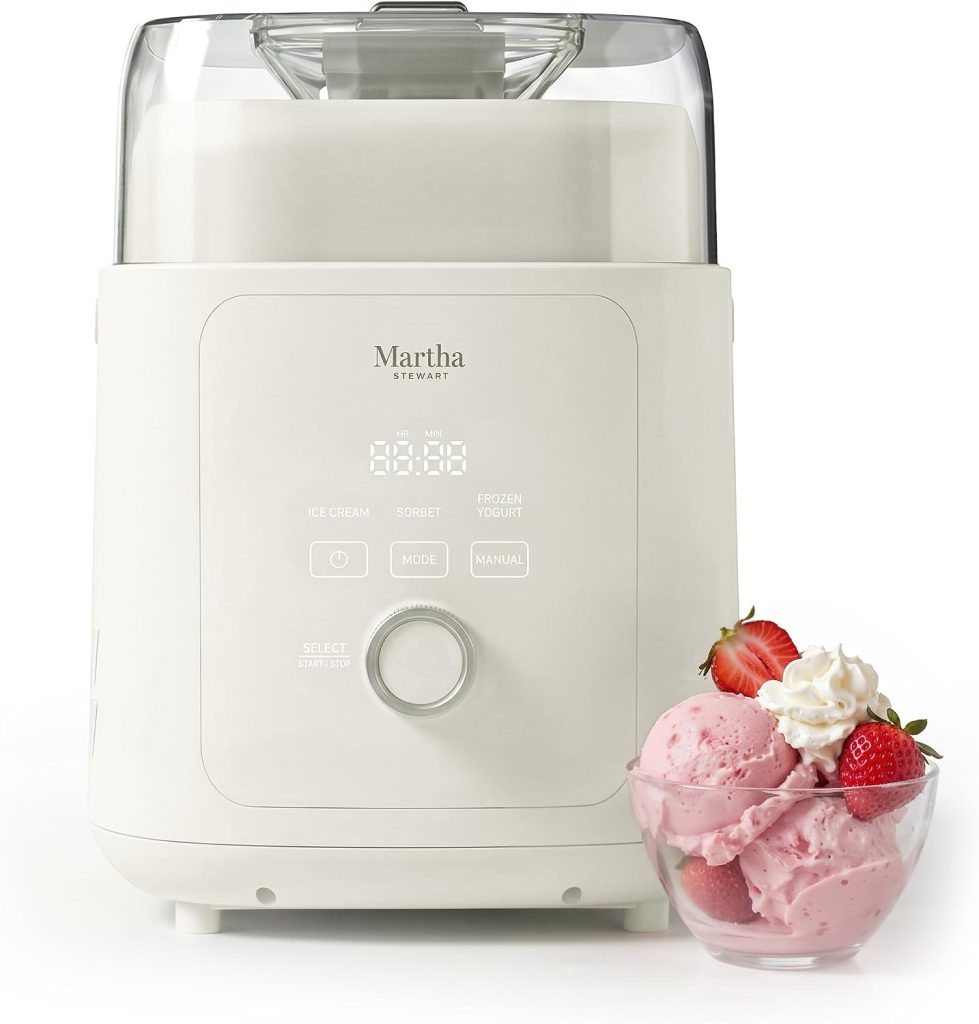 White Martha Stewart ice cream maker with digital controls, reminiscent of the innovative Ninja Creami, alongside a glass bowl filled with strawberry ice cream, whipped cream, and fresh strawberries.