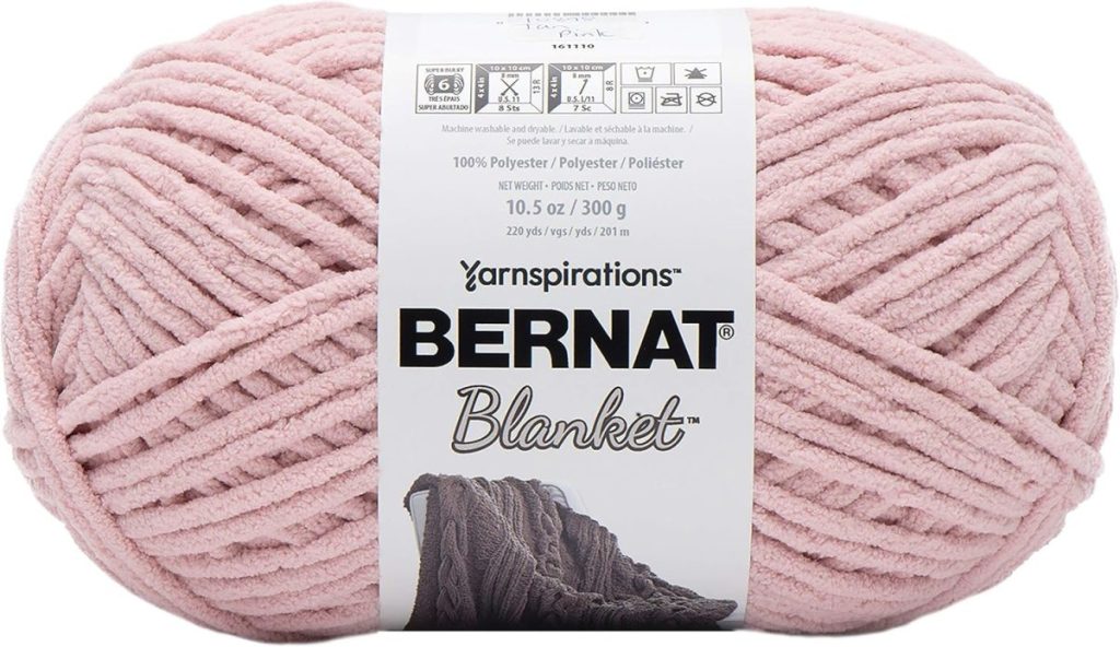 A skein of Bernat Blanket yarn in light pink, perfect for Creative Crafts, showing the product label with fiber content and care instructions.