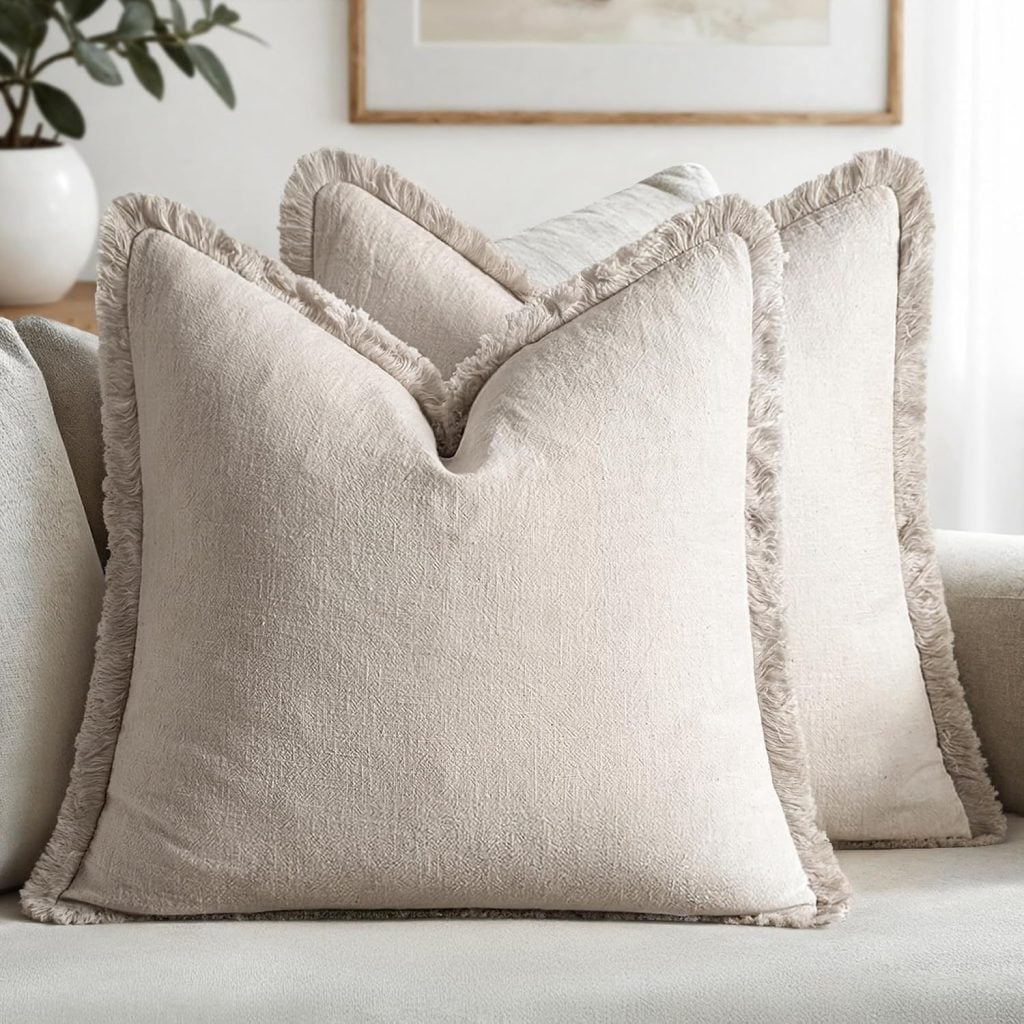 Two beige throw pillows with fringed edges are placed side by side on a light-colored sofa in a modern living room, creating a cozy spot for summer sleep and relaxation.