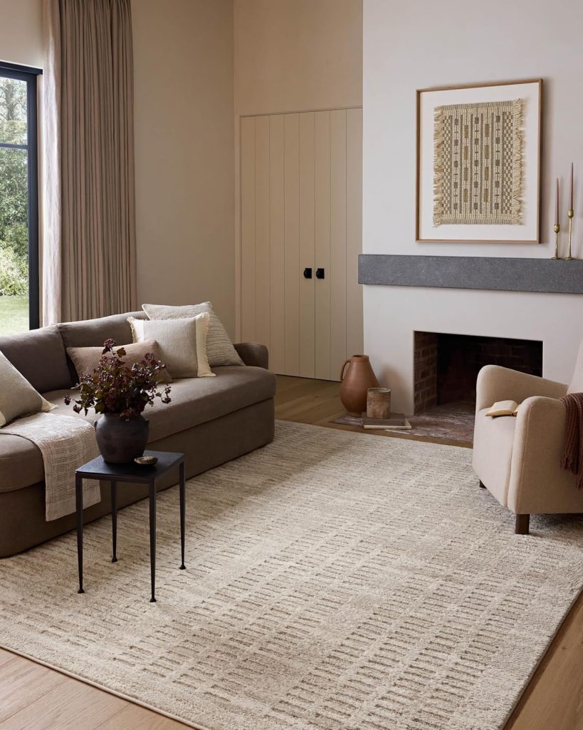 A neutral-toned living room with a beige sofa, armchair, light patterned rug, small black side table, fireplace, and framed artwork on the wall—perfect inspiration for your next Amazon Prime Day home refresh.