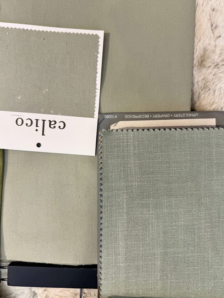 Two samples of light green upholstery fabric with serrated edges, one labeled "Calico" and the other displayed in a swatch book, laid on a textured surface.