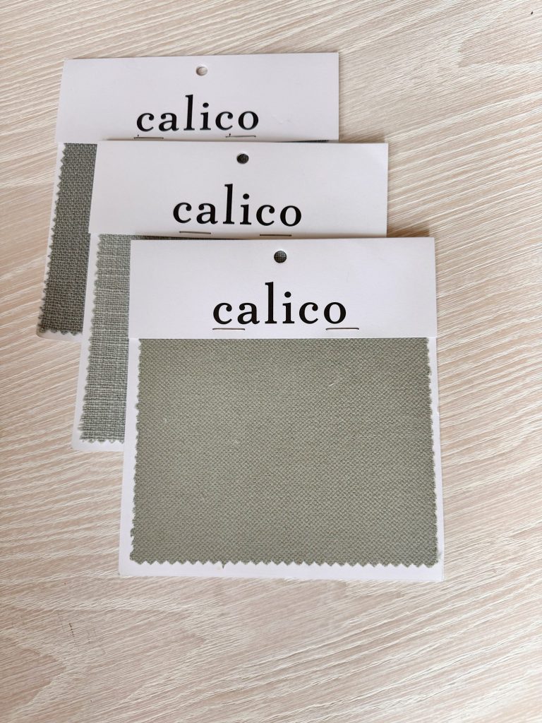 Three fabric swatches labeled "calico" are displayed on a light wood surface, each showing a textured, pale sage green material.