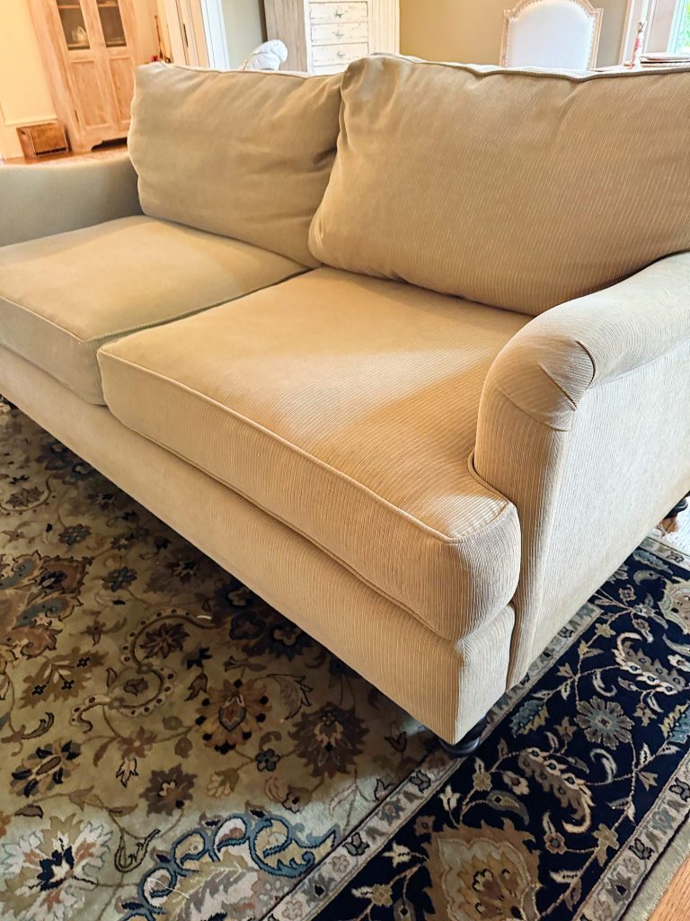 A beige corduroy sofa with two seat cushions and two back cushions sits on a patterned area rug in a living room.
