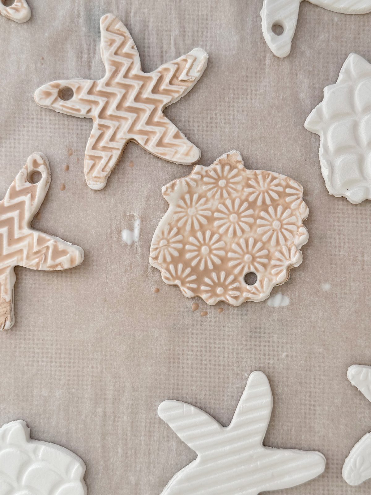 Various white clay ornaments with textured patterns, including starfish and a floral round shape, are arranged on a parchment-lined surface.