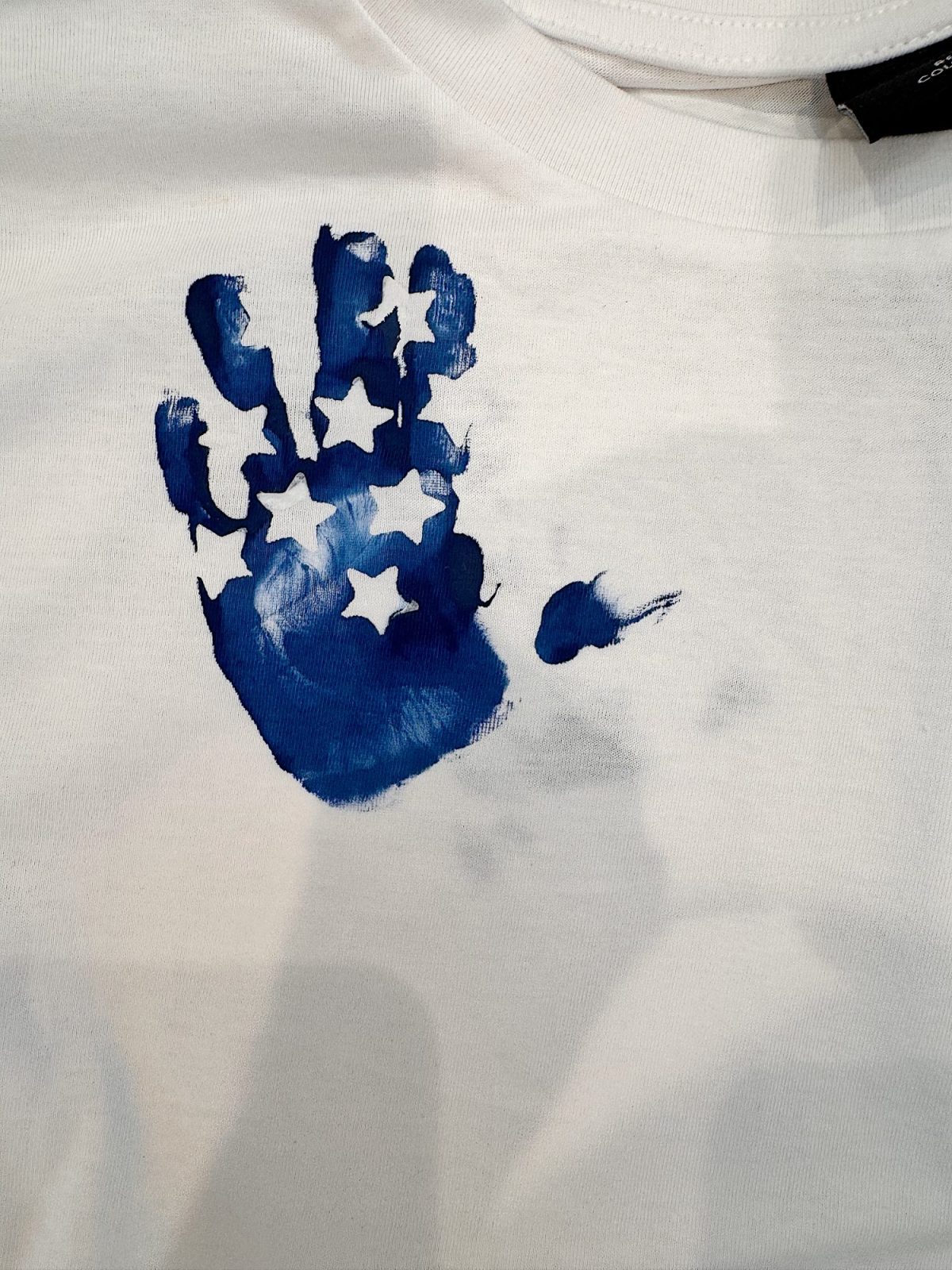 A blue handprint with white star shapes appears on a white fabric background.