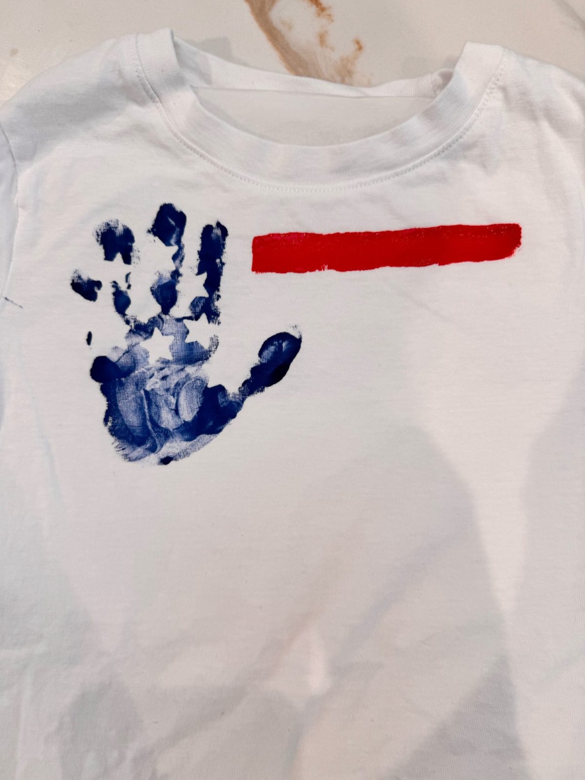 A white t-shirt with a blue handprint and a horizontal red stripe painted next to it.