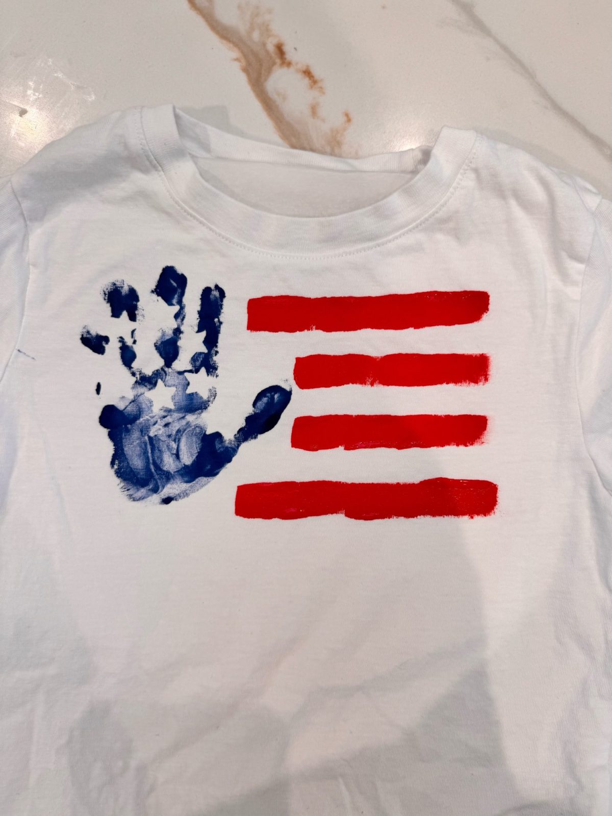 A white shirt with a blue handprint and four horizontal red stripes painted on it, resembling a stylized American flag.