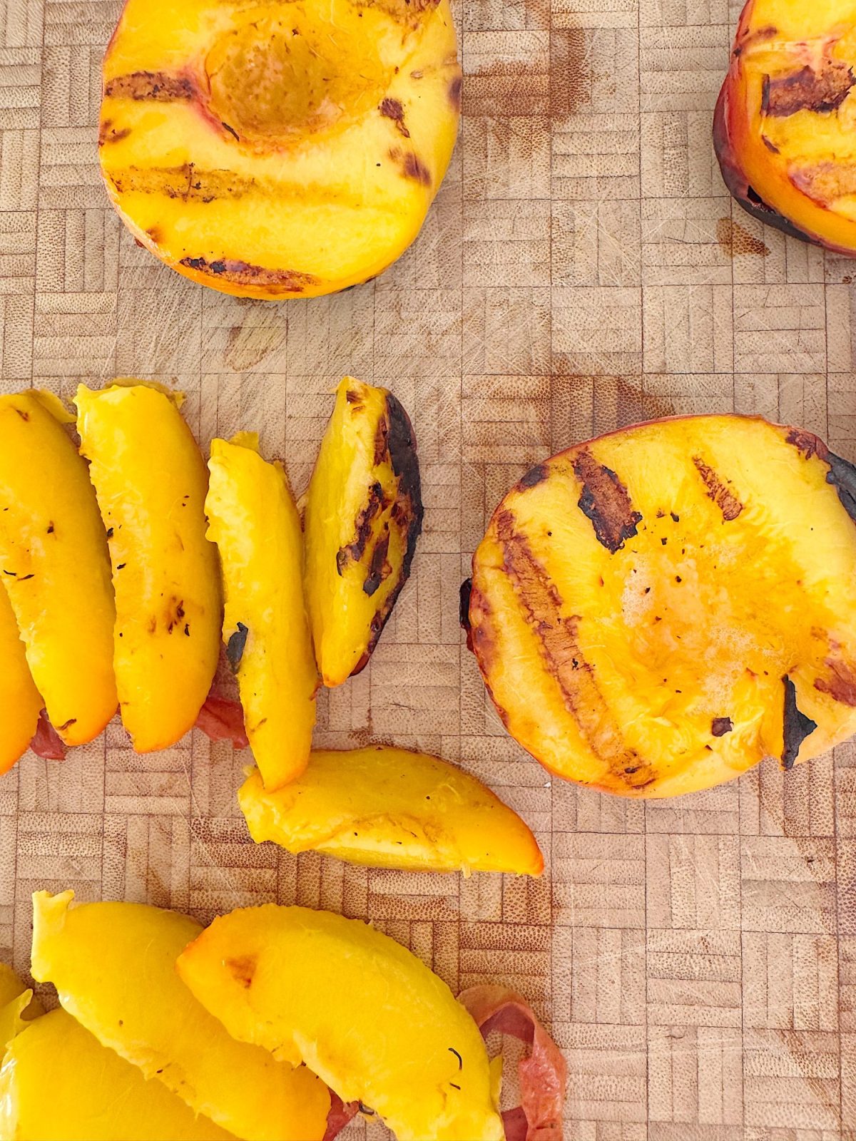Grilled peach halves and slices on a wooden cutting board, showing grill marks and a golden-yellow color.