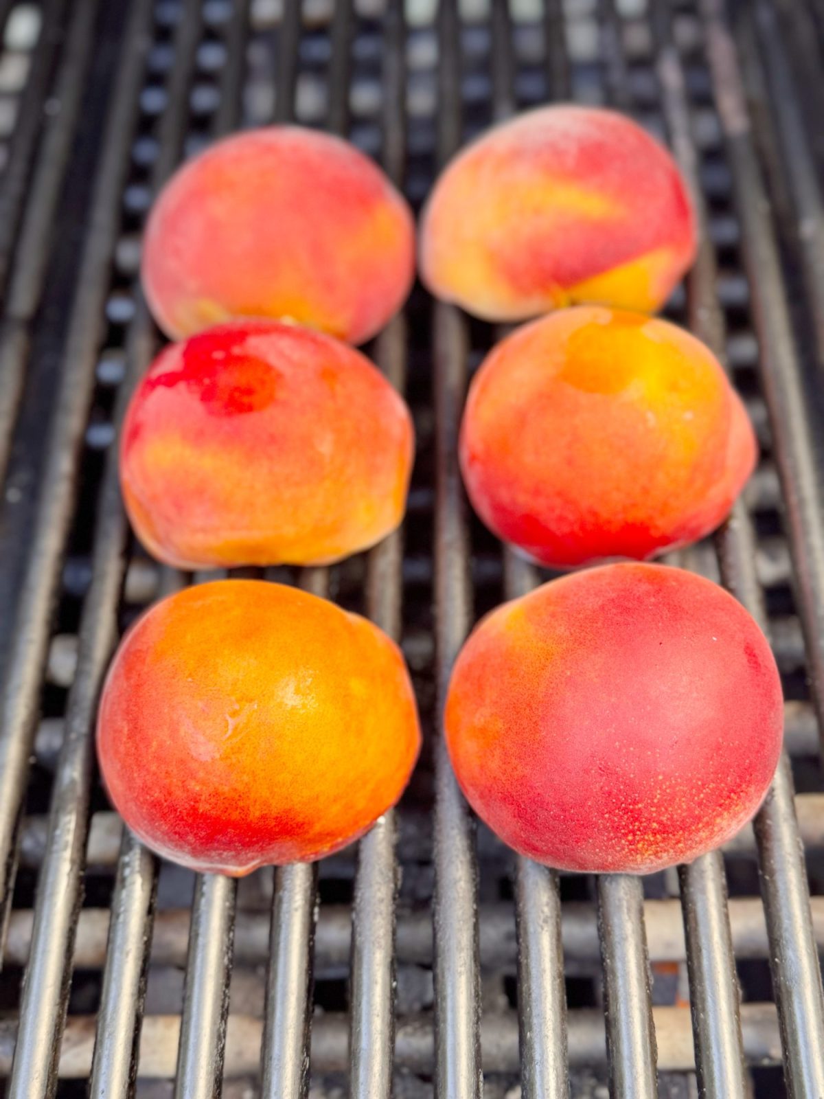 Six whole peaches are placed on a grill with metal bars, ready to be cooked.