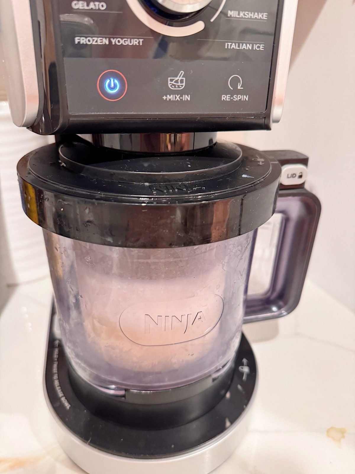 A Ninja ice cream maker is processing ingredients with the "Frozen Yogurt" setting selected. The machine's container is frosted and locked in place.