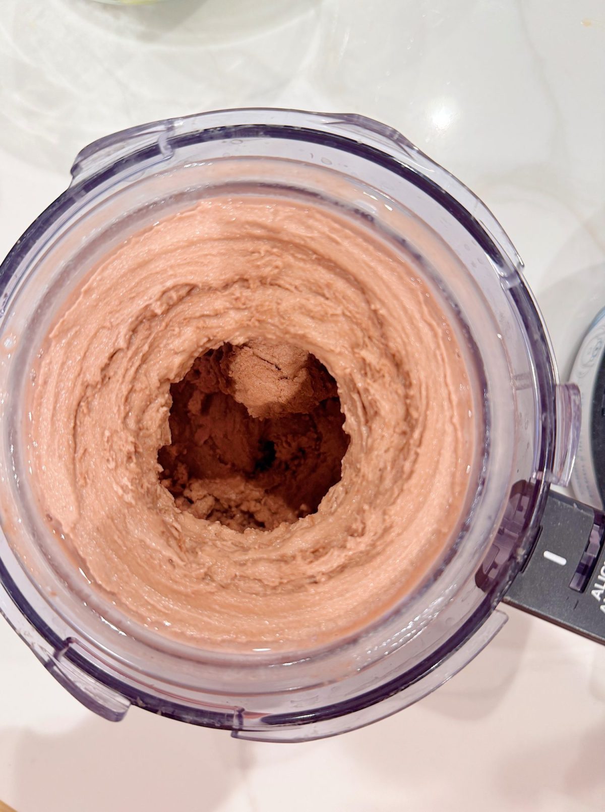 A top-down view of a food processor containing thick, whipped chocolate mixture with a hollow center.