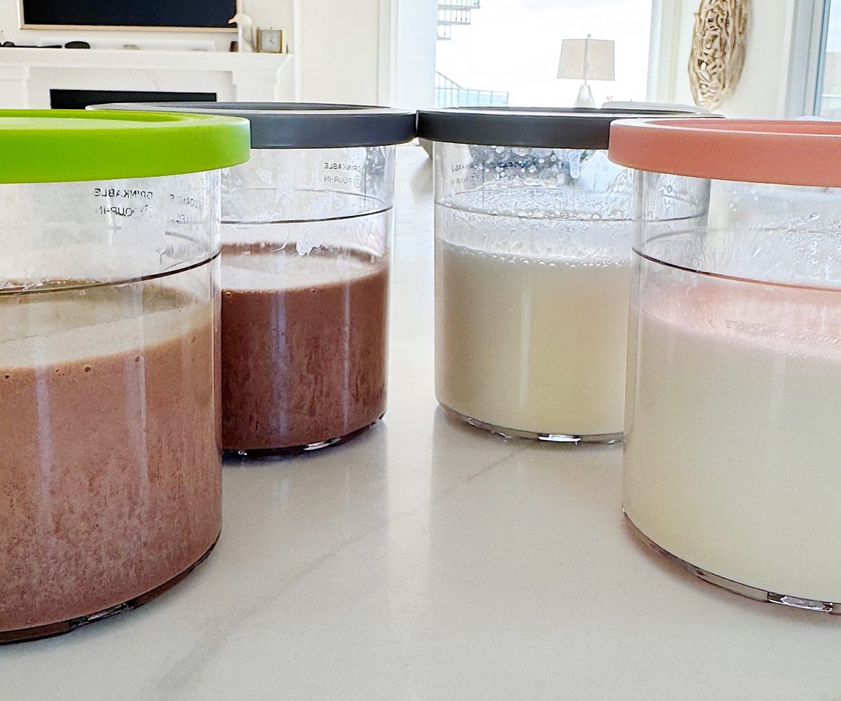 Four clear containers with colorful lids are filled with different liquids or mixtures, placed on a white kitchen counter.