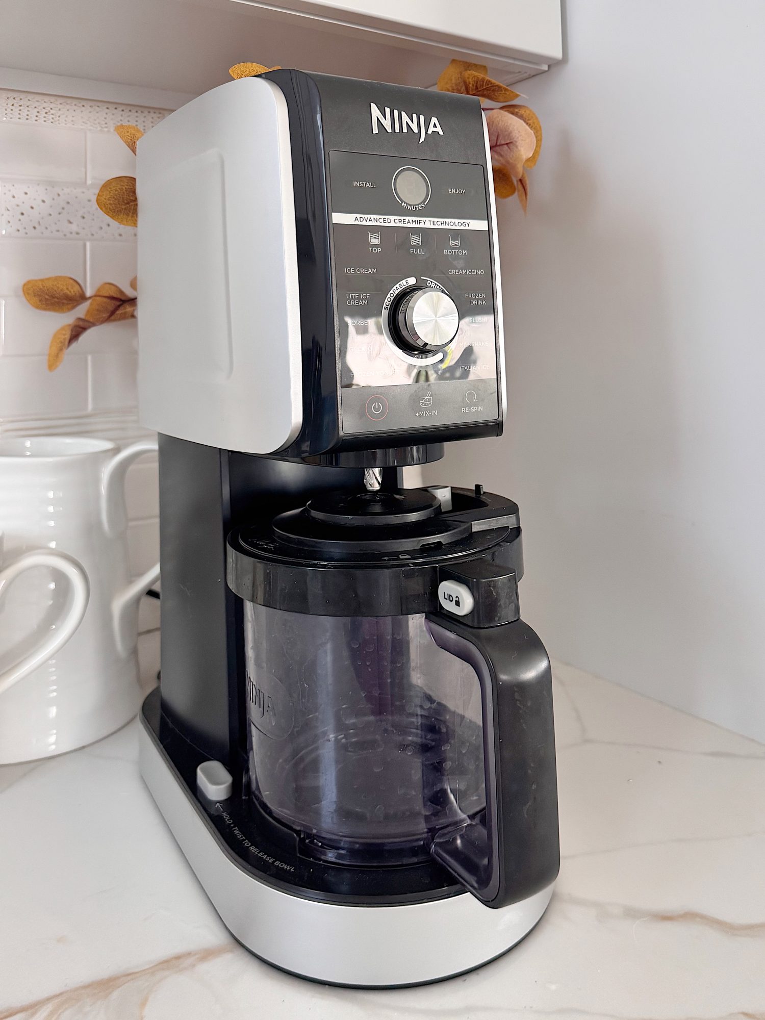 A Ninja coffee maker with a glass carafe sits on a kitchen countertop next to white ceramic containers.