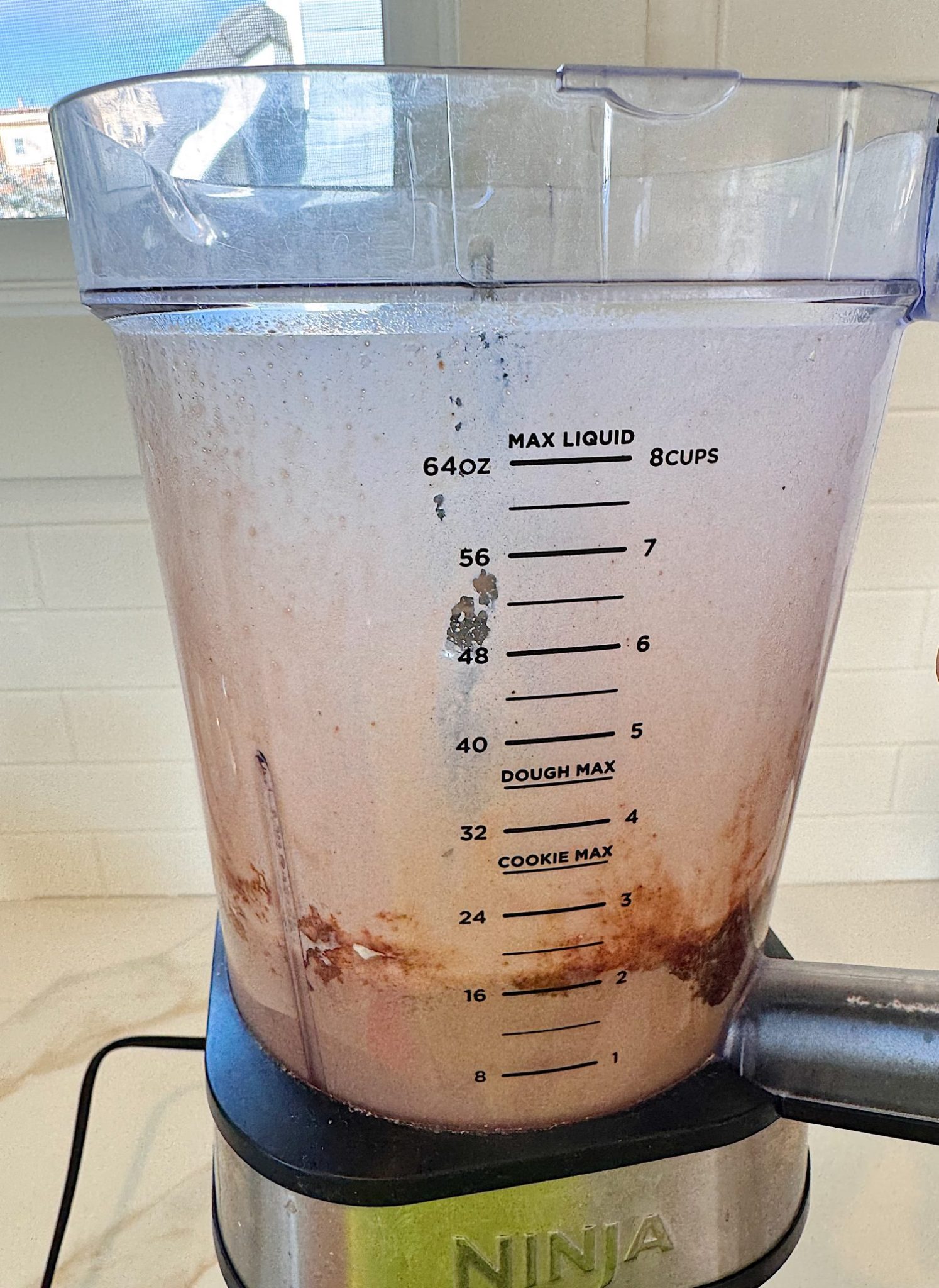 A blender filled with a light brown liquid mixture, some ingredients settled at the bottom, sits on a kitchen countertop.