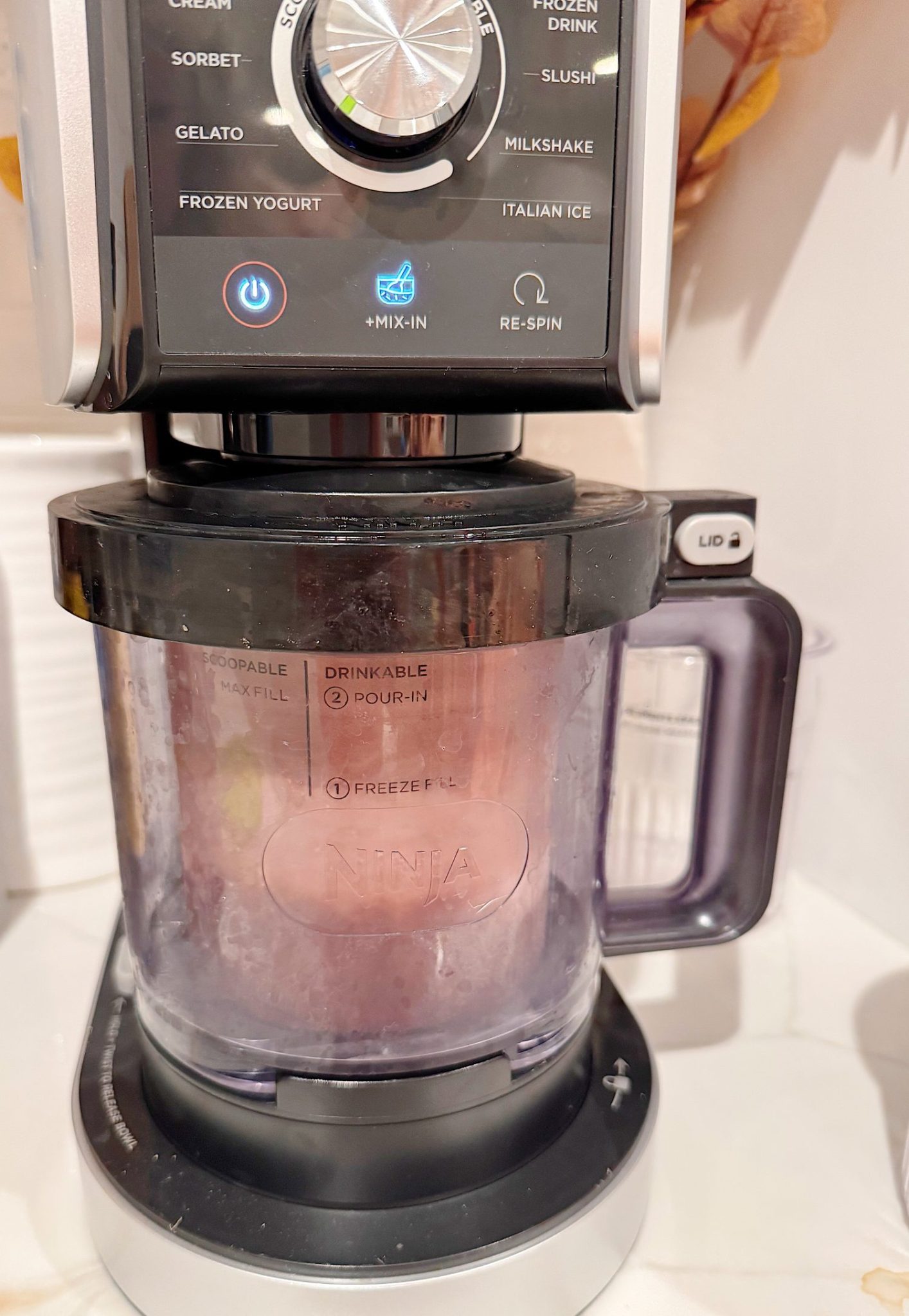 A Ninja ice cream maker in operation, blending a frozen mixture inside a clear container with visible ice crystals.
