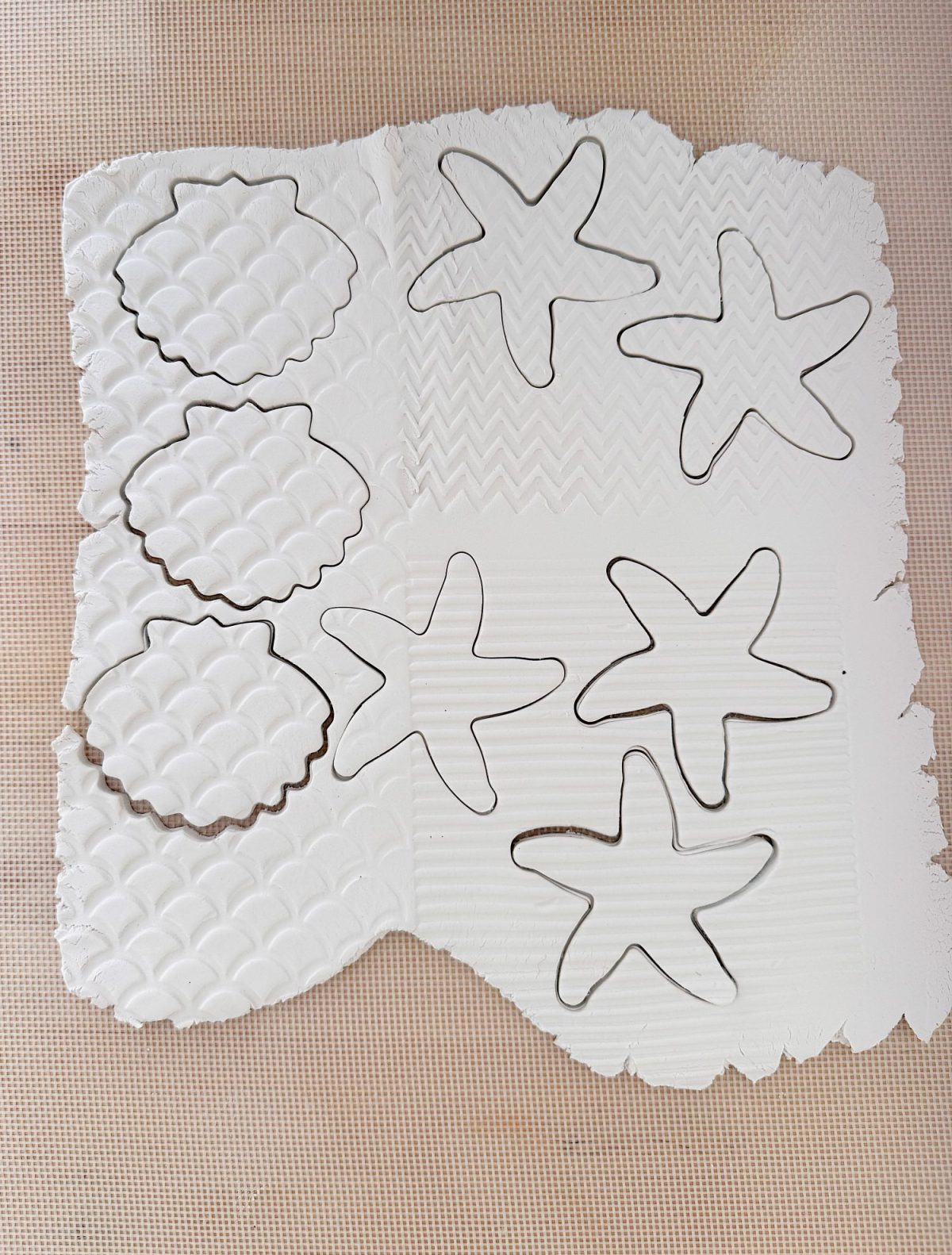 A sheet of white clay with starfish and scalloped circle shapes cut out, featuring textured patterns on the surface.