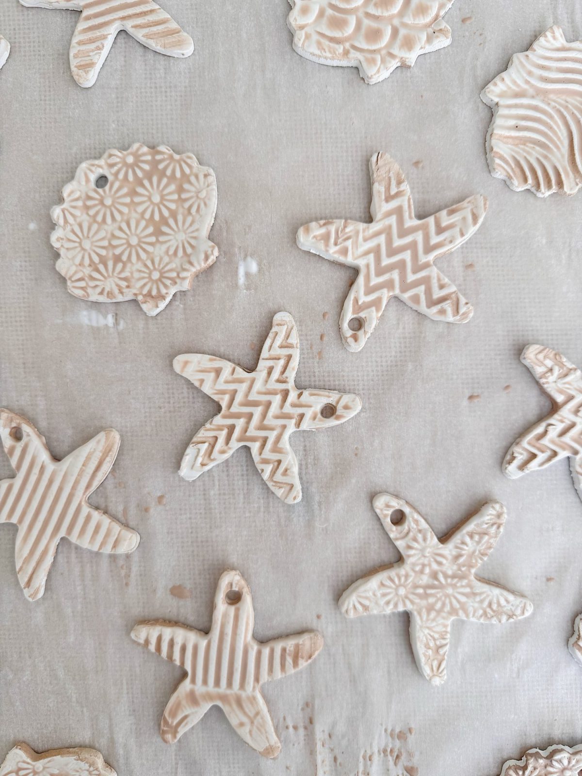 Assorted star and round-shaped clay ornaments with textured patterns and holes for hanging, arranged on a white surface.
