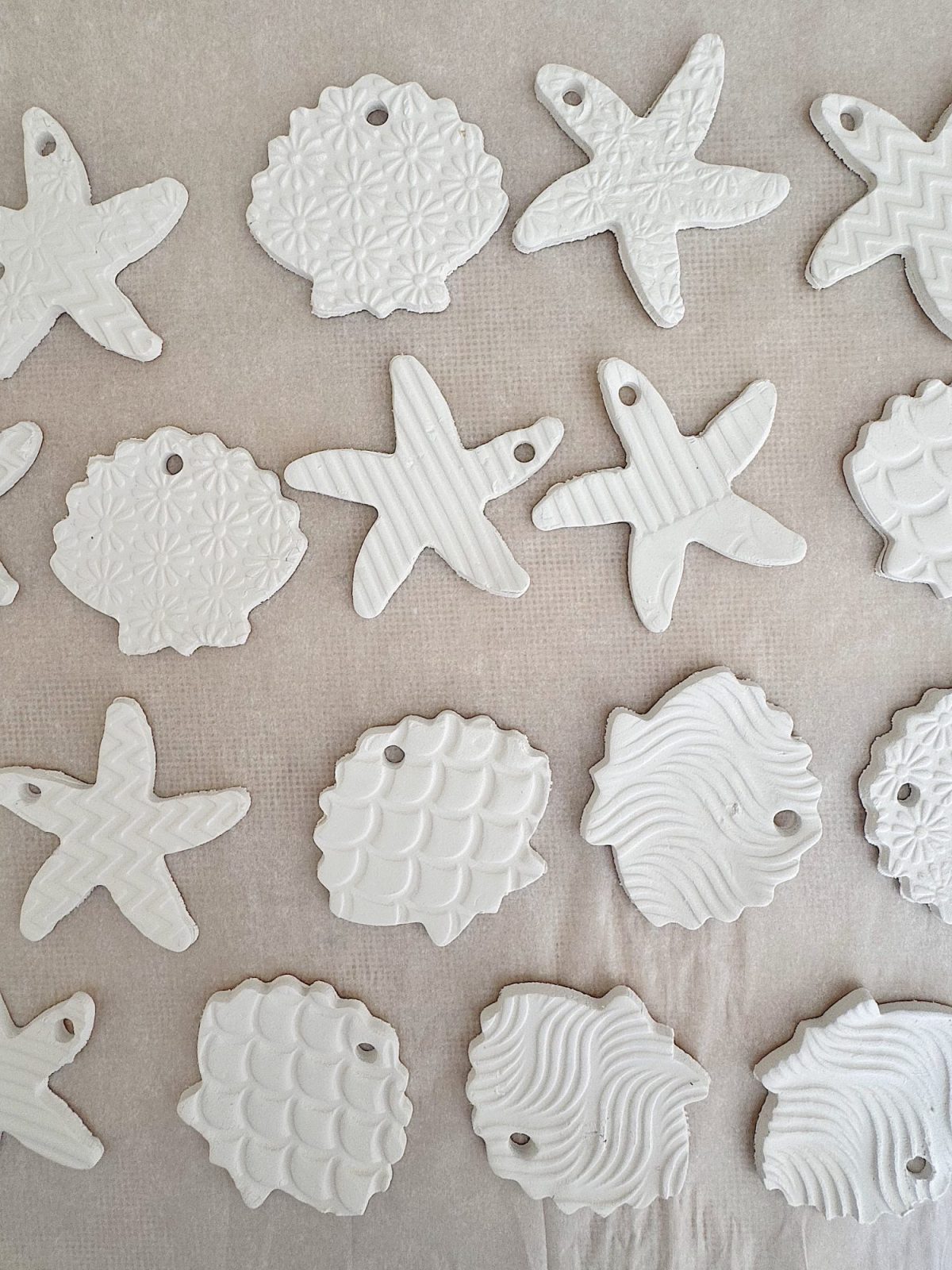 White clay ornaments in the shapes of starfish and shells with various textured patterns are arranged on a parchment-lined surface.