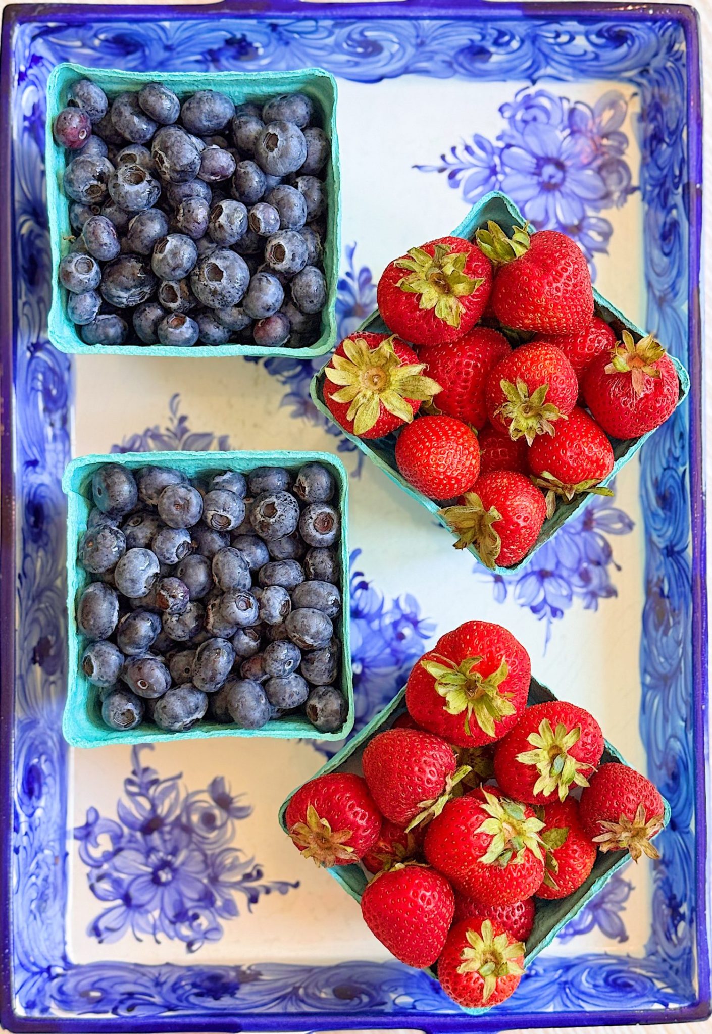 Three small cartons of fresh blueberries and strawberries are arranged on a decorative blue and white floral tray.