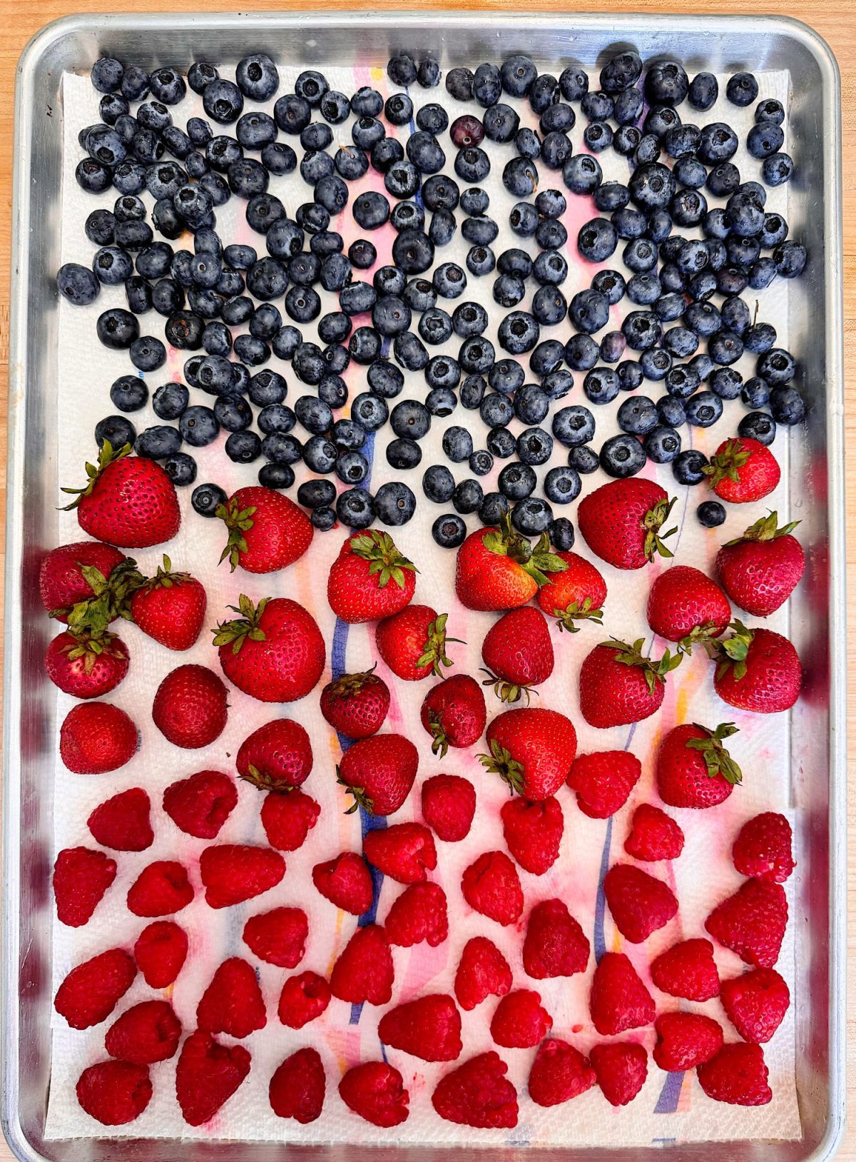 A baking sheet with rows of blueberries, strawberries, and raspberries arranged by type on a paper towel.