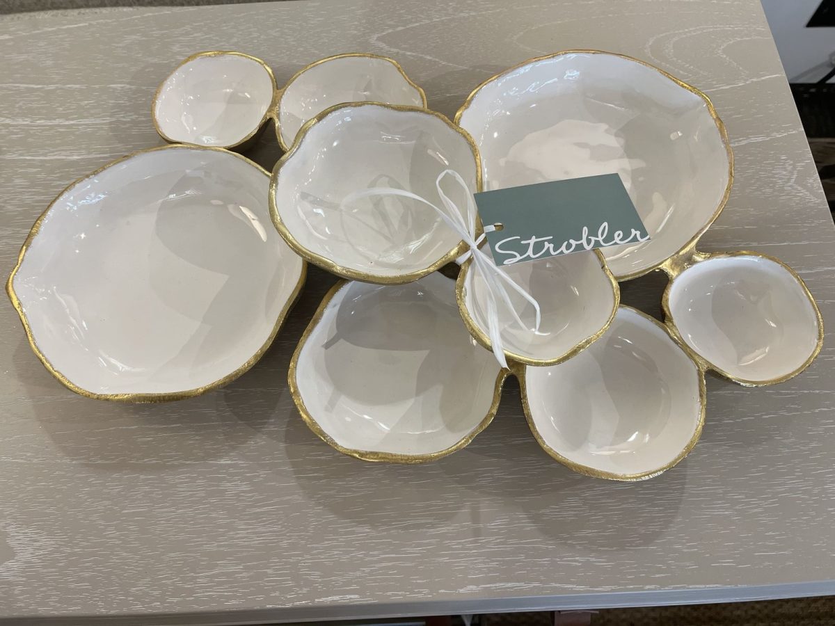 A set of white ceramic bowls with gold rims arranged on a light wood surface, labeled with a tag reading "Strobler.
