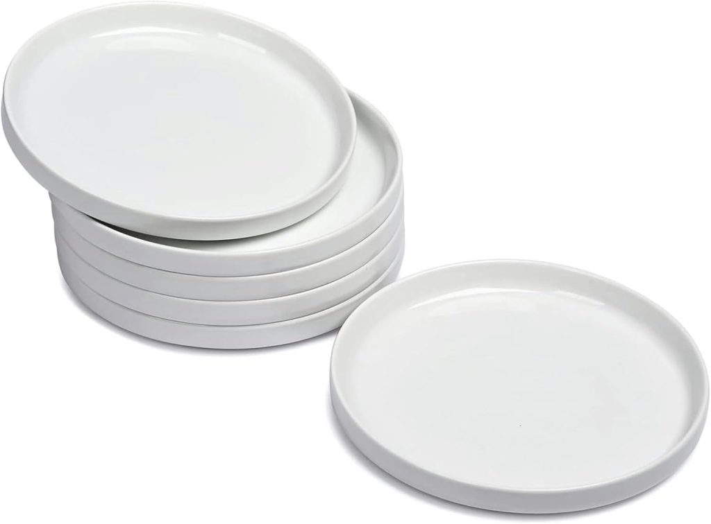 A stack of six plain white ceramic plates, with one plate lying separately in front of the stack.