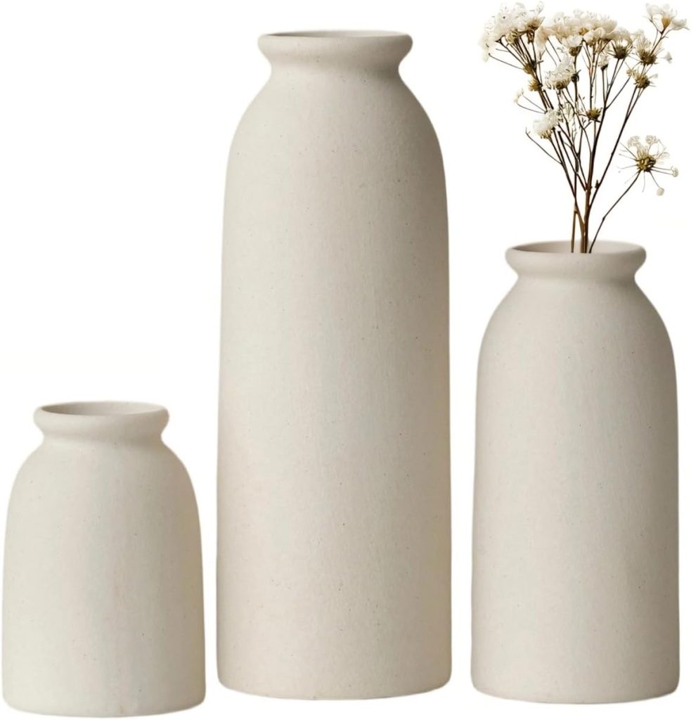 Three matte white ceramic vases of varying heights; the tallest contains a small arrangement of white baby's breath flowers.