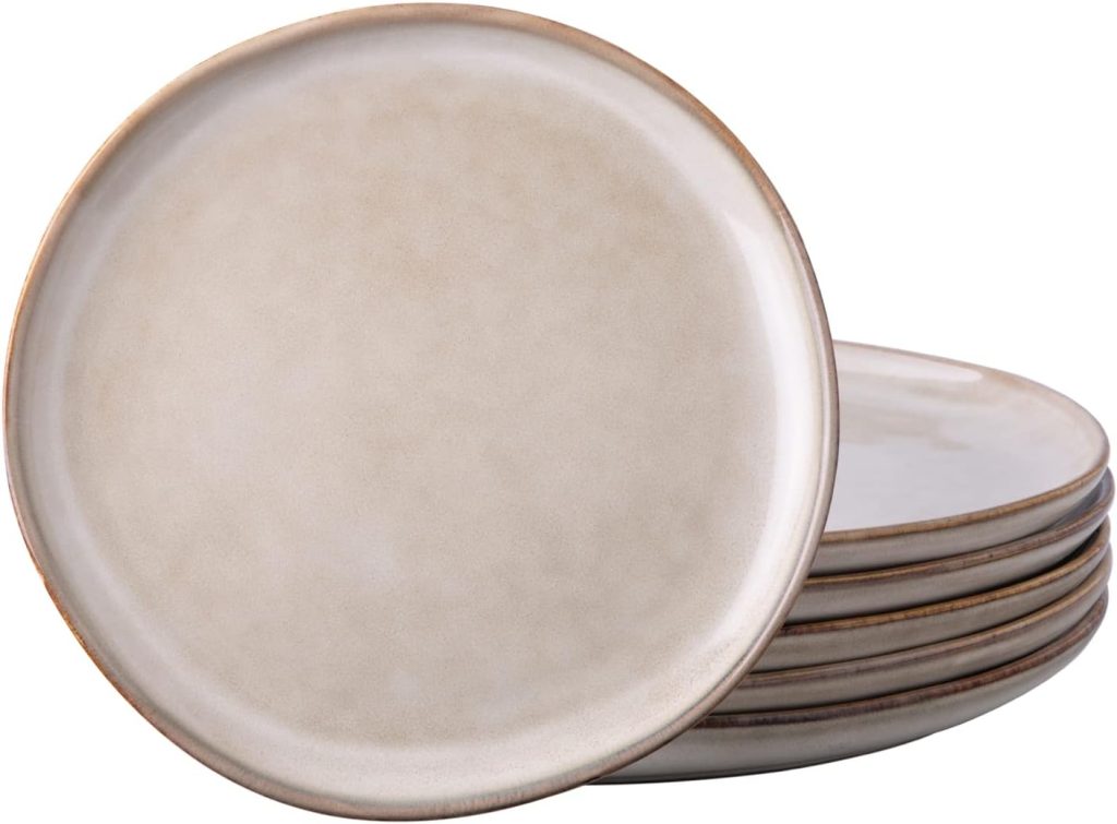 A stack of six round, beige ceramic plates with a slight brown rim, carefully crafted from handmade clay, with one plate upright in front of the others.