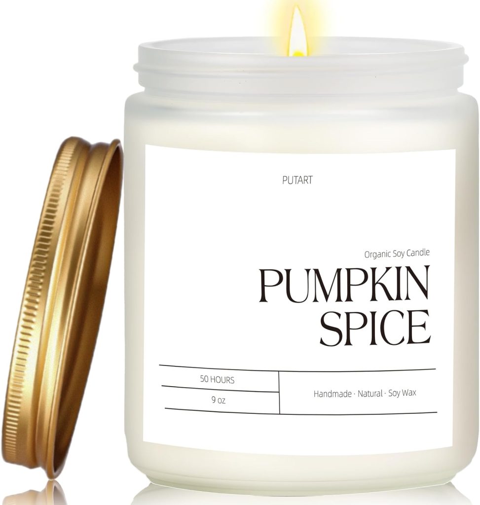 A lit white pumpkin spice soy candle in a glass jar with a gold lid placed beside it; the label reads “PUMPKIN SPICE” and notes it is handmade and lasts 50 hours.