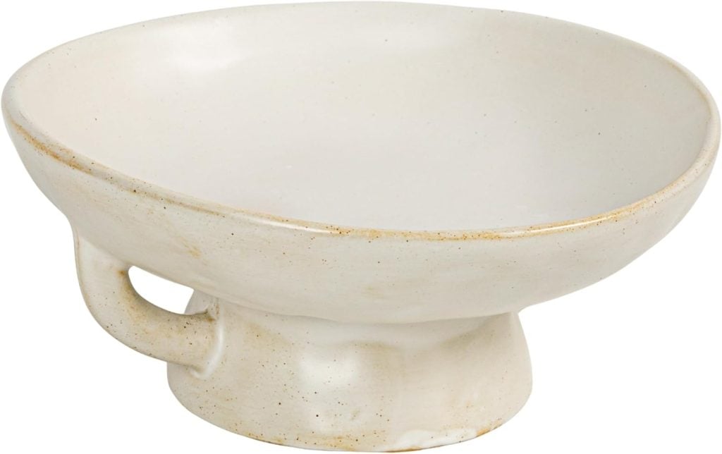 A white ceramic bowl with a short pedestal base and a small side handle, featuring a slightly uneven, handmade appearance.