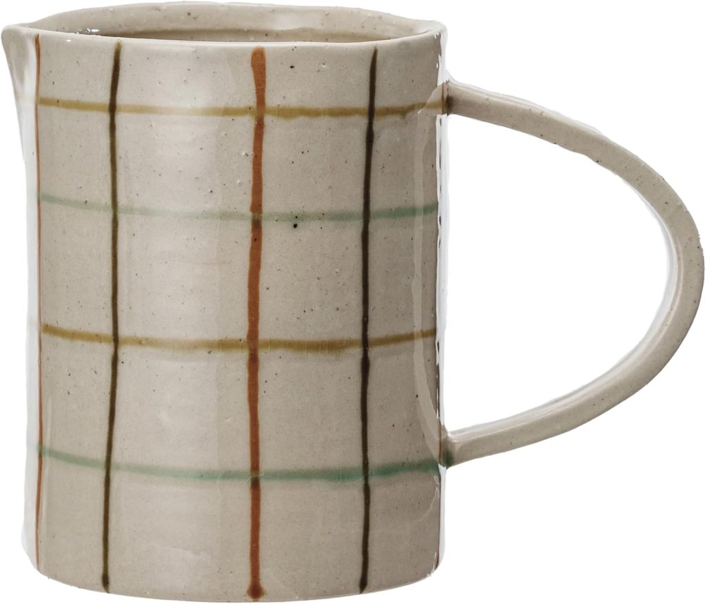A ceramic pitcher with a large handle and a beige base, featuring a simple grid pattern in brown, green, and rust-colored lines.